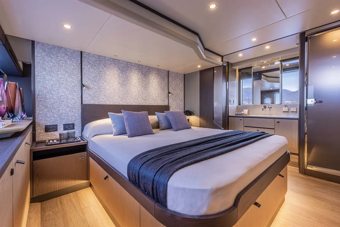 Modern bedroom featuring a large bed with decorative cushions, stylish furnishings, and an en-suite bathroom with a mirror.
